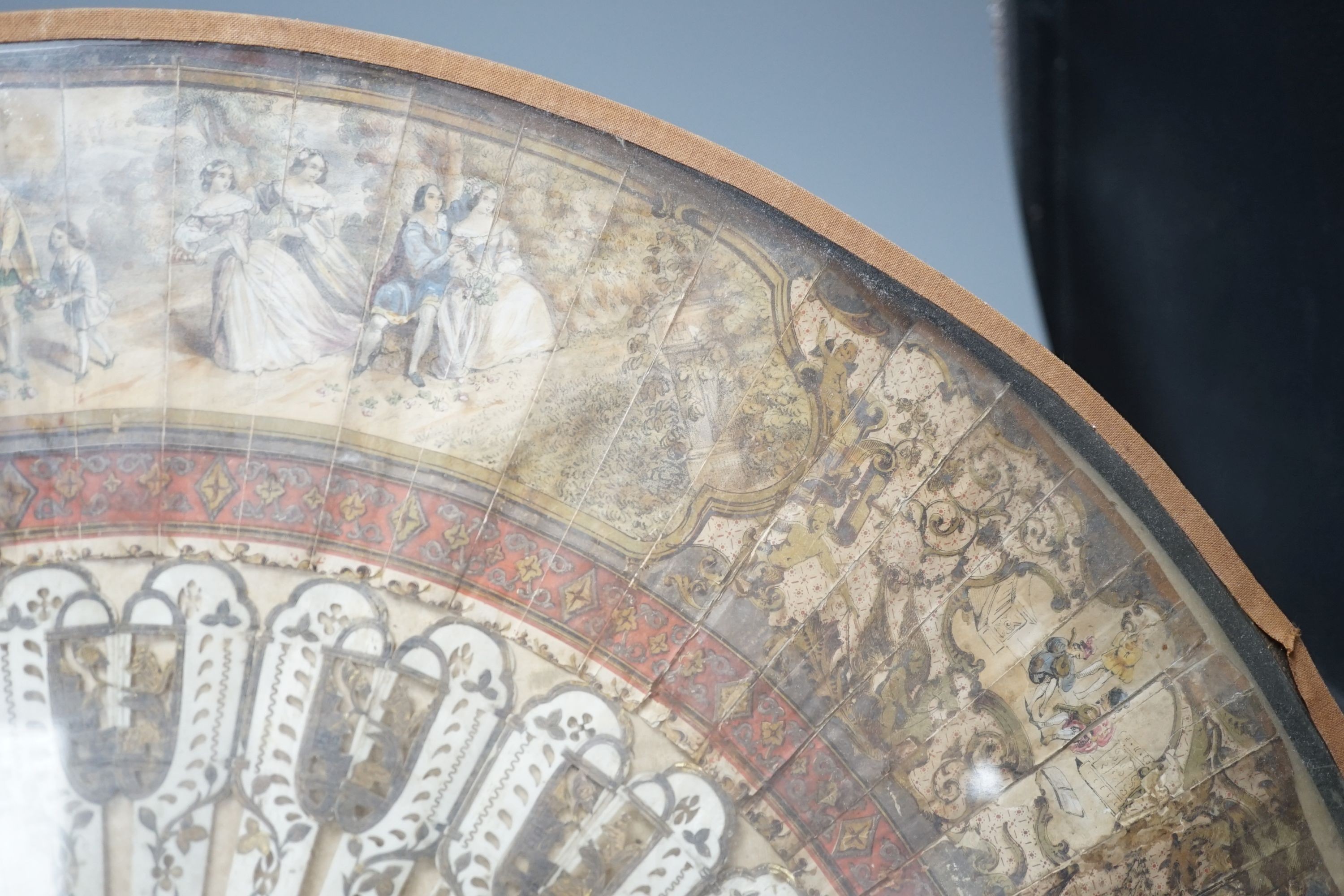 A cased 19th century French lithograph paper leaf and bone stick fan, 56 cms wide.
